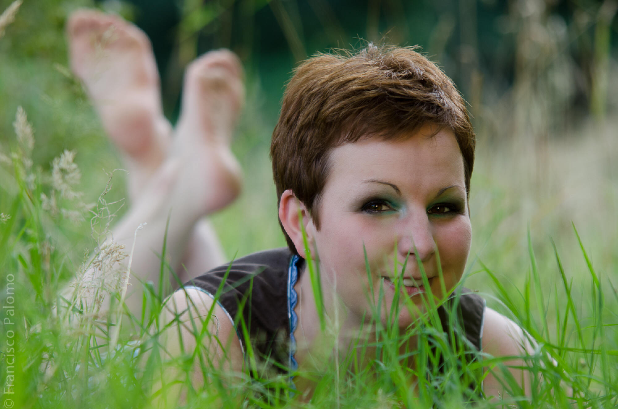 Frau liegt bäuchlings im Gras, die nackten Füße in der Luft